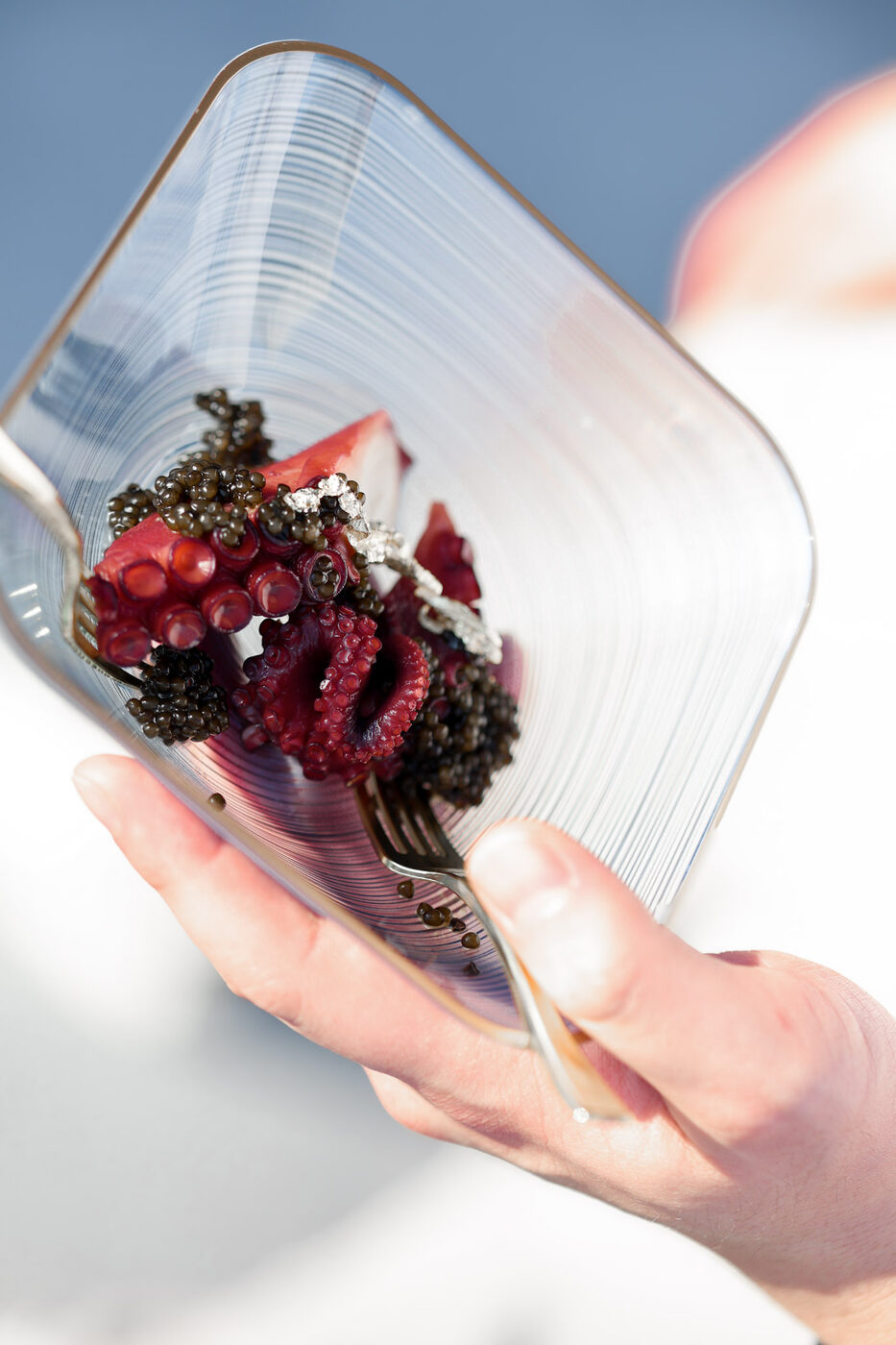A glass plate of octopus crowned with caviar, held up to the light