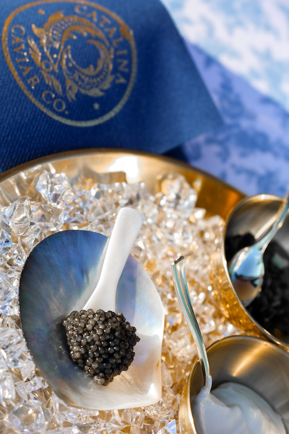 Caviar on a mother-of-pearl spoon over crushed ice, beside a navy napkin embroidered with the Catalina crest