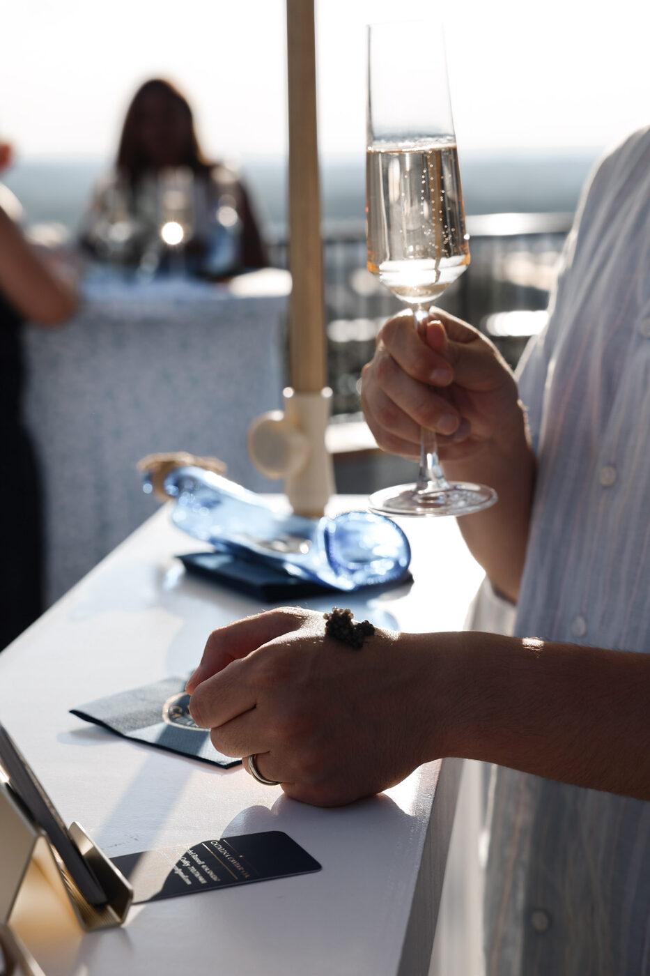 A guest holding a flute of champagne rests a caviar bump on the back of their hand at a Catalina rooftop cart